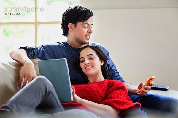 Junges Paar mit digitalem Tablett und Mobile auf dem Wohnzimmersofa