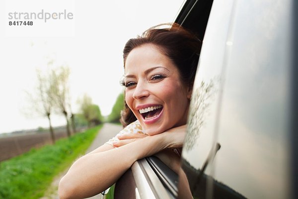 Junge Frau  die sich aus dem Autofenster lehnt und lacht.