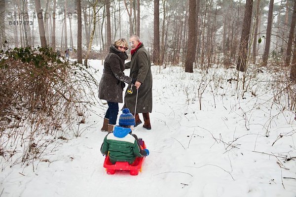 Großeltern ziehen Enkel auf Schlitten im Schnee