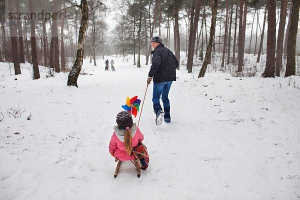 Vater zieht Tochter auf Schlitten im Schnee