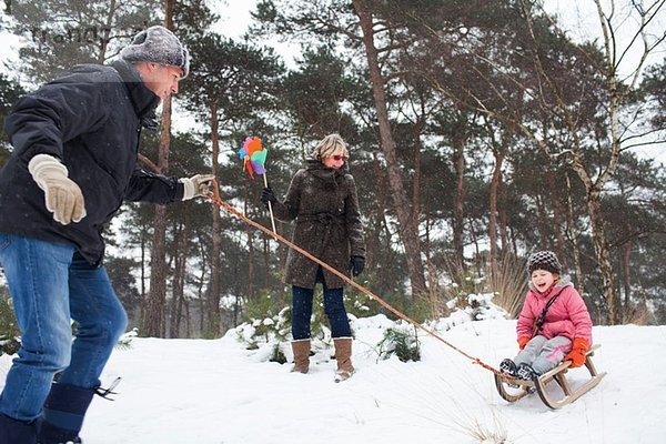 Vater und Großmutter ziehen Mädchen auf Schlitten im Schnee