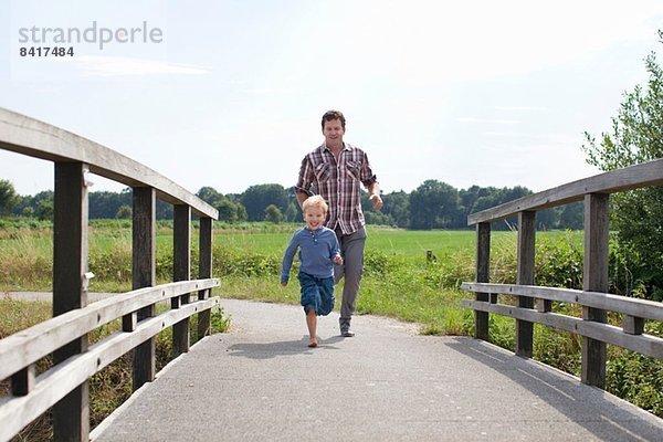 Vater und Sohn laufen über Holzbrücke