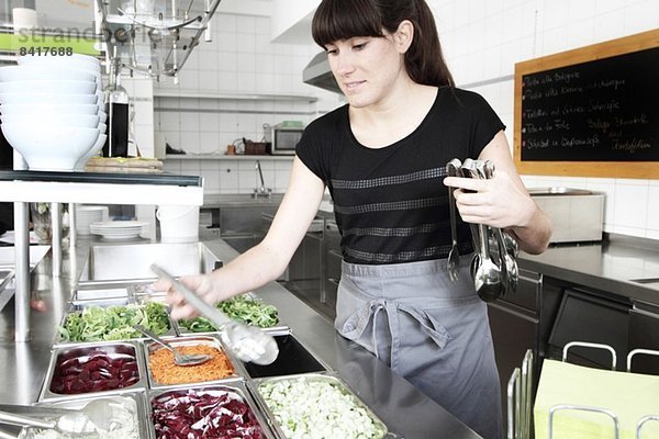 Frau  die in der Restaurantküche arbeitet und eine Salatzange hält