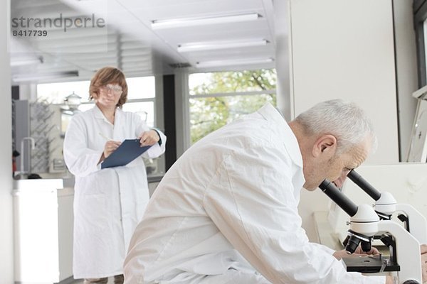 Wissenschaftler  die im Labor arbeiten  Mann  der durchs Mikroskop schaut und Frau  die Notizen macht.