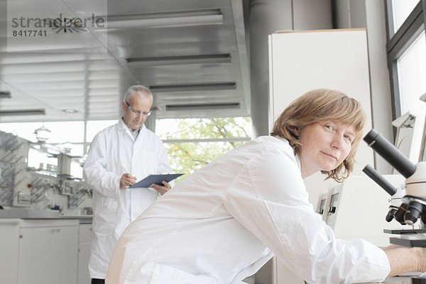 Wissenschaftler im Labor  Frau mit Mikroskop und Mann beim Notieren