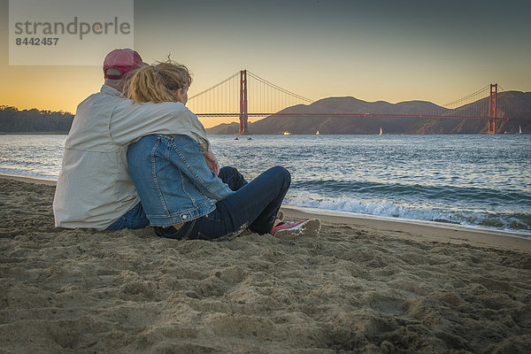 USA  Kalifornien  San Francisco  reifes Paar am Strand an der Golden Gate Bridge bei Dämmerung