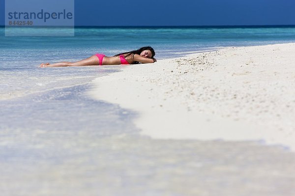 Malediven  Junge Frau im Bikini im flachen Wasser liegend