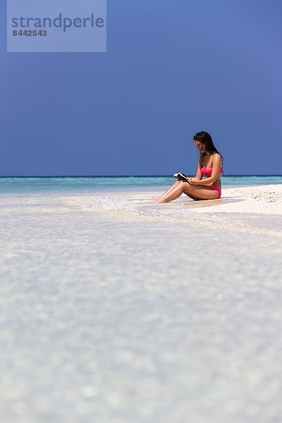 Malediven  Junge Frau im Bikini sitzend im Flachwasser Lesebuch