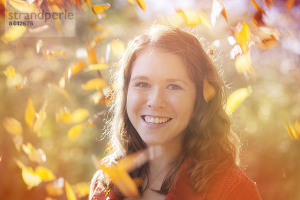 Porträt einer glücklichen jungen Frau mit wirbelnden Herbstblättern um sie herum  Nahaufnahme