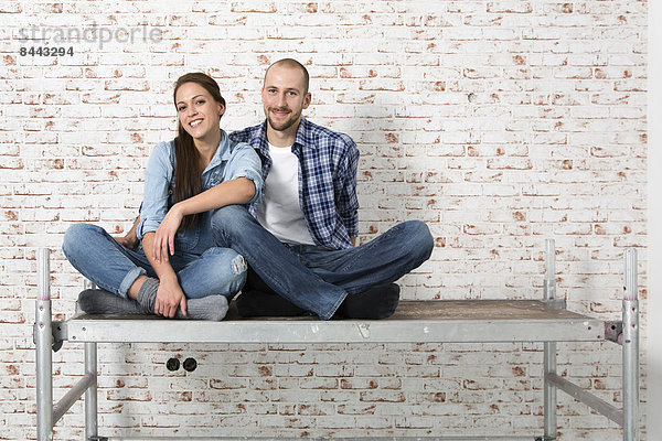 Junges Paar  das in ein neues Zuhause einzieht  auf einem Gestell sitzend