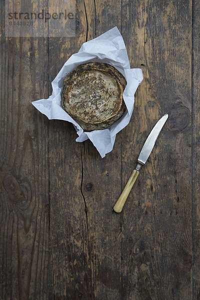 Tomme de Savoie Käse auf fettdichtem Papier  Messer auf Holztisch