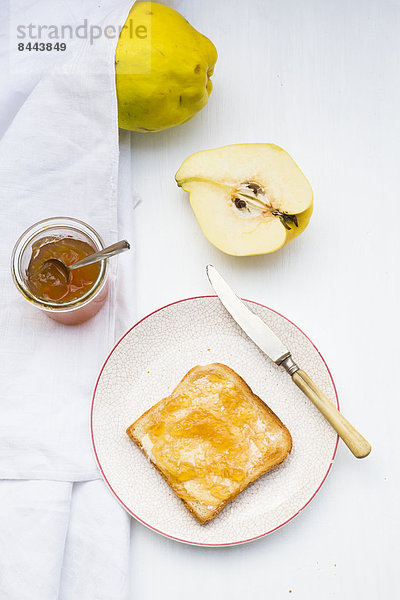 Quinces (Cydonia oblonga)  selfmade quince jelly and slice of toast on white wooden table