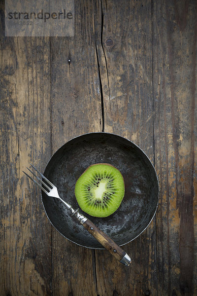 Bowl with half of a kiwi (Actinidia deliciosa) and a fork on wooden table