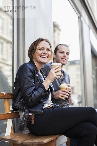 Glückliches Paar trinkt Kaffee in Einwegbechern auf der Bank auf dem Bürgersteig