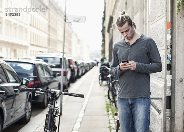 Junger Mann SMS über Handy  während er auf dem Bürgersteig steht.