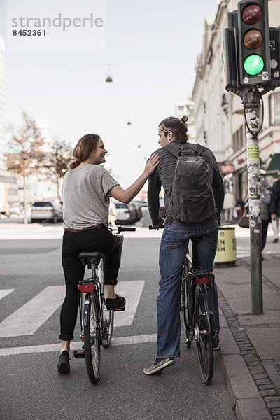 Rückansicht des Paares mit Fahrrädern  die an der Zebrastraße warten.