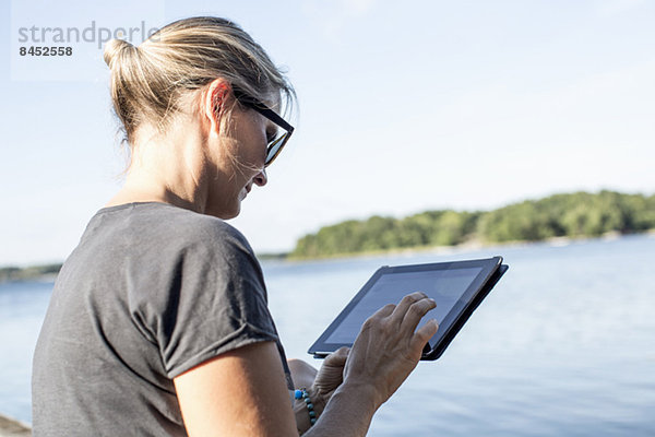Mittlere erwachsene Frau mit digitalem Tablett am See