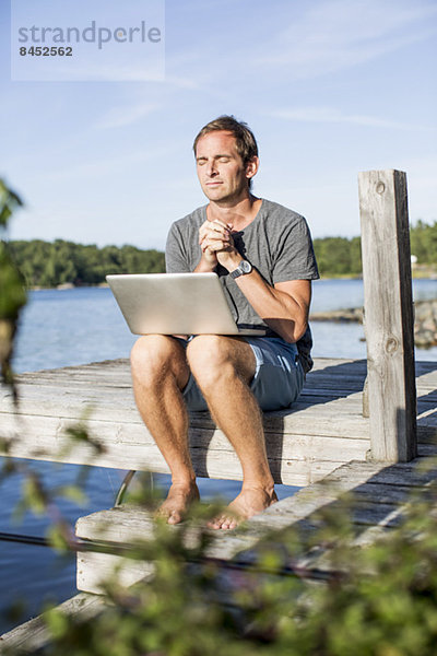 Erwachsener Mann beim Beten mit Laptop am Pier