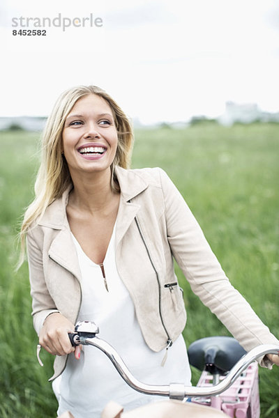 Fröhliche junge Frau mit dem Fahrrad schaut weg  während sie auf dem Feld steht.