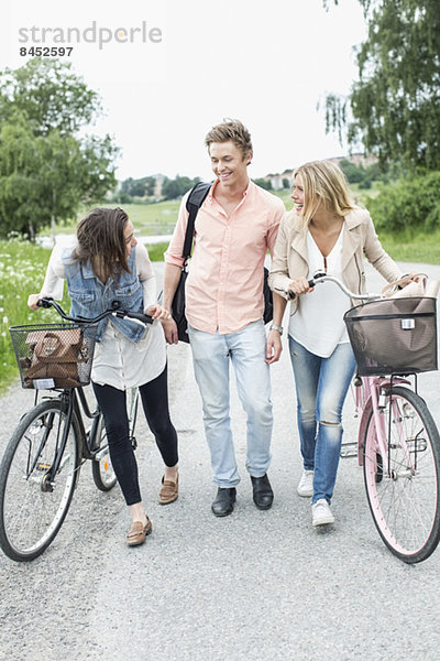 Glückliche junge Freunde mit Fahrrädern auf der Landstraße