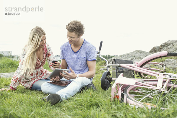 Junges Paar mit Handy und digitalem Tablett per Fahrrad auf dem Feld