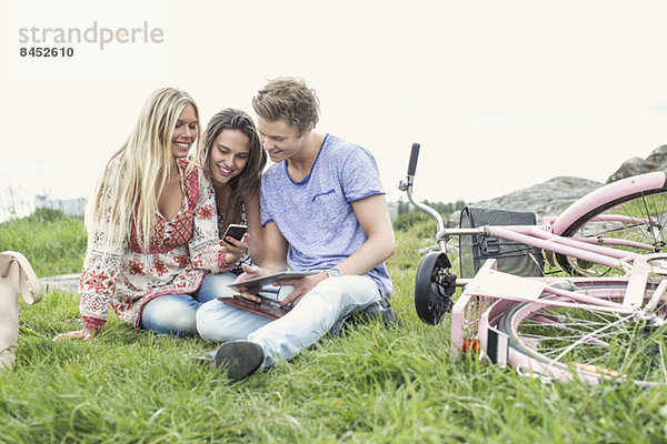 Junge Freunde mit Handy und digitalem Tablett per Fahrrad auf dem Feld