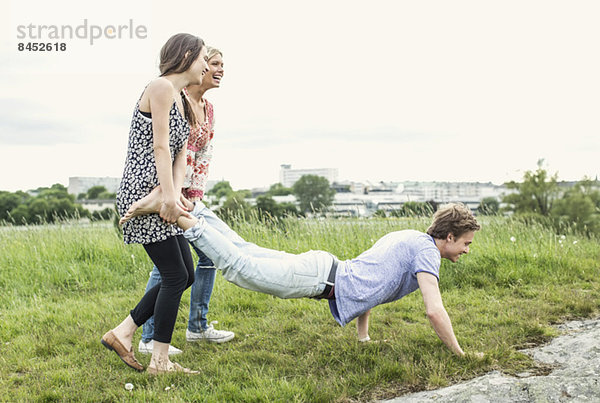 Fröhliche junge Frauen mit männlichen Freunden  die auf dem Feld Liegestütze machen.