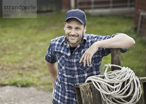 Lächelnder Bauer schaut weg  während er sich auf das Geländer auf dem Bauernhof stützt.