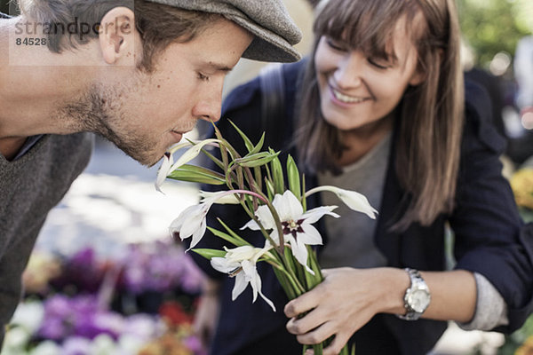 Junger Mann riecht Blumen  die von einer Frau auf dem Markt gehalten werden.