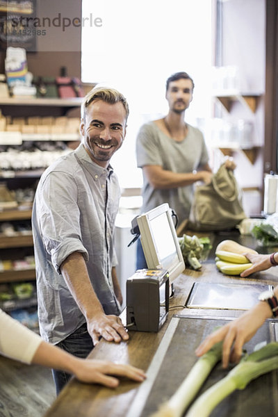 Lächelnder Mann an der Supermarktkasse mit Freund im Hintergrund