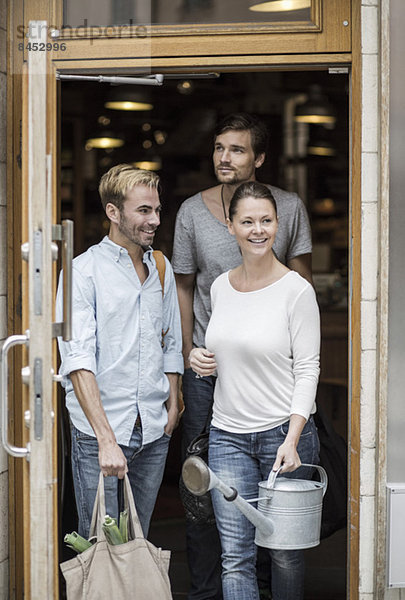 Freunde mit Lebensmitteln und Gießkanne verlassen den Supermarkt