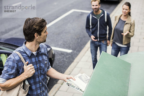 Mann  der Zeitung in den Papierkorb legt  während er Freunde auf dem Bürgersteig betrachtet