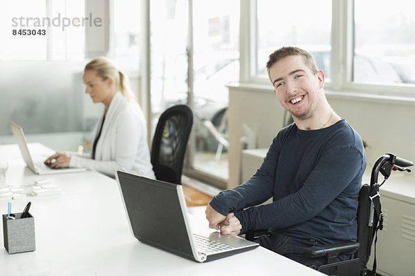 Portrait eines glücklichen Geschäftsmannes mit zerebraler Lähmung mit Laptop im Büro