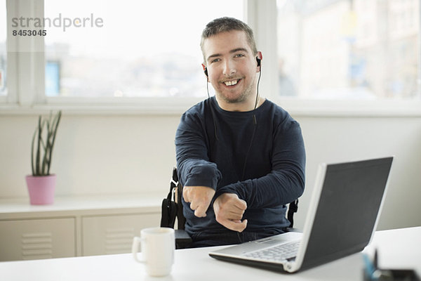 Portrait eines glücklichen behinderten Geschäftsmannes mit Laptop am Schreibtisch im Büro