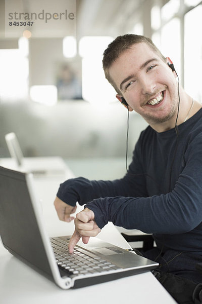 Porträt eines glücklichen Geschäftsmannes mit zerebraler Lähmung am Laptop beim Musikhören