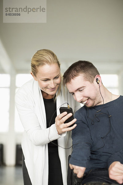 Hausmeisterin unterstützt behinderten Mann bei der Nutzung des Mobiltelefons zu Hause