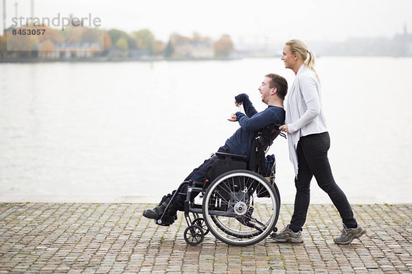 Hausmeister schiebt behinderten Mann im Rollstuhl entlang des Sees