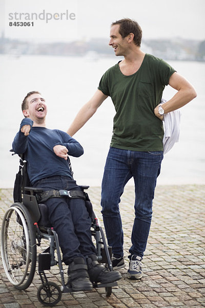 Hausmeister mit einem glücklichen behinderten Mann im Rollstuhl am See.