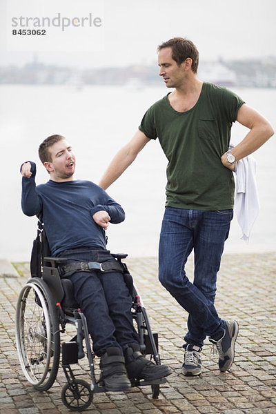 Behinderter Mann im Rollstuhl mit männlichem Hausmeister am See