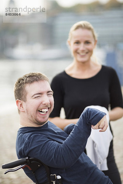 Behinderter Mann im Rollstuhl lacht durch Hausmeister im Freien