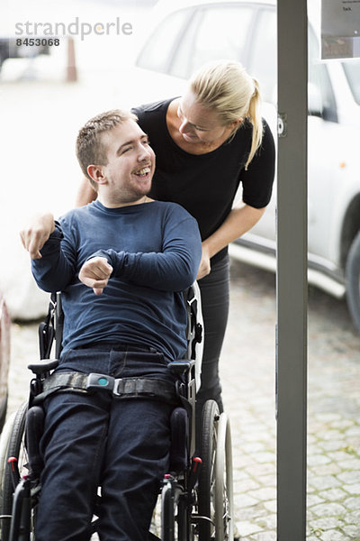 Hausmeister im Gespräch mit behinderten Menschen im Rollstuhl im Freien