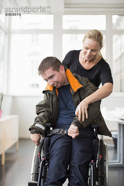 Hausmeisterin hilft behinderten Mann im Rollstuhl zu Hause