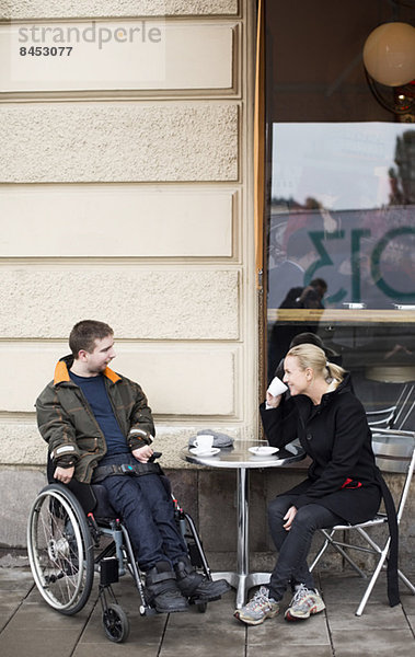 Hausmeisterin und behinderter Mann beim Kaffeetrinken im Straßencafé