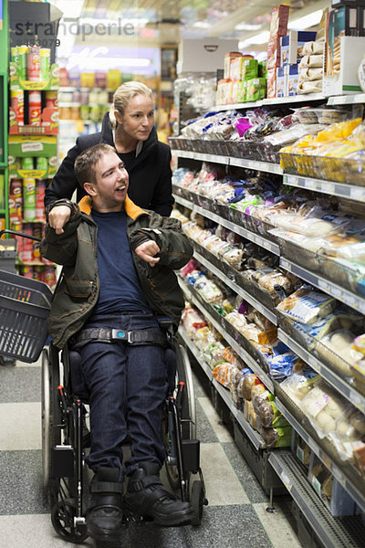 Behinderter Mann im Rollstuhl mit Hausmeisterin im Supermarkt