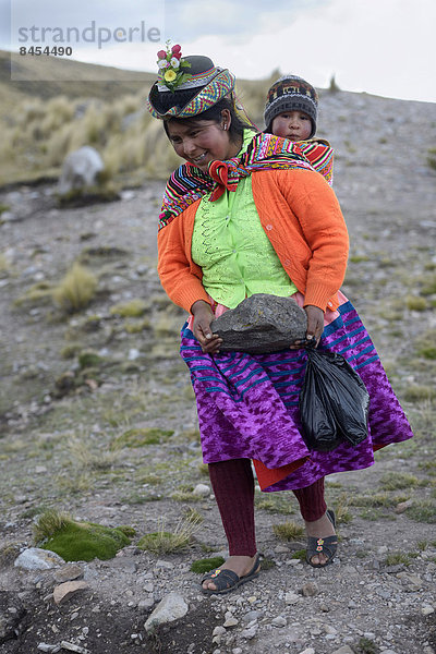 Junge Frau mit Kind im Tragetuch schleppt einen schweren Stein  um damit das Ufer eines künstlichen Sees zur Feldbewässerung zu sichern  Quispillacta  Ayacucho  Peru