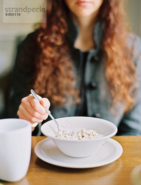 Eine Frau  die Frühstücksflocken aus einer weißen Schüssel isst.