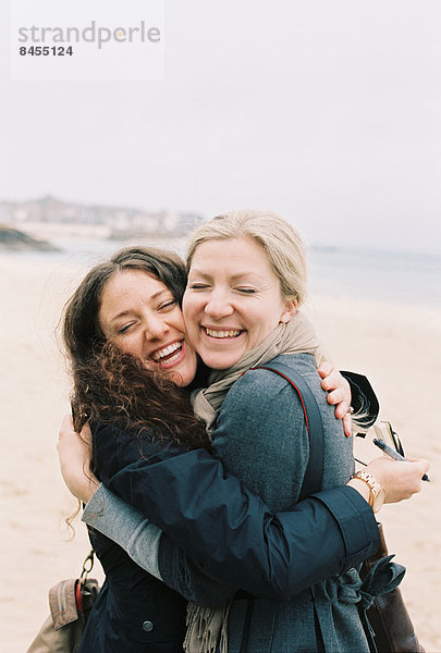 Zwei Frauen  die sich am Strand Wange an Wange umarmen.