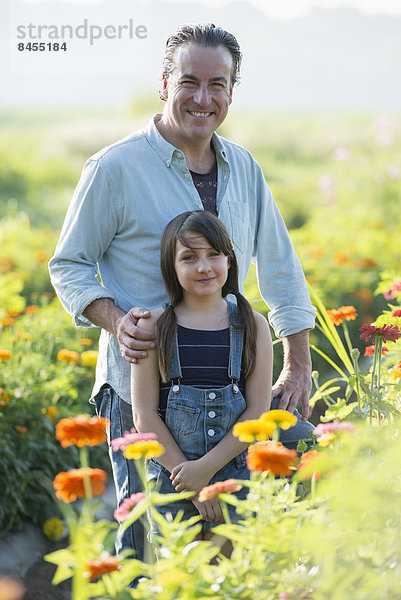 Sommer auf einem Biobauernhof. Ein Mann und ein Mädchen in einem Blumenfeld.