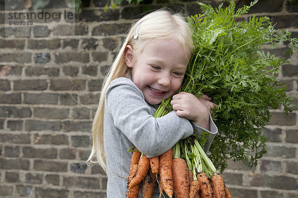 Ein junges Mädchen hält einen großen Karottenstrauß in der Hand.