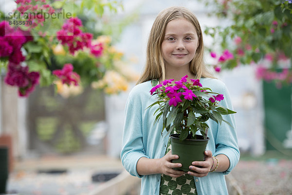 Eine Bio-Blumenpflanzengärtnerei. Ein junges Mädchen hält eine blühende Pflanze.